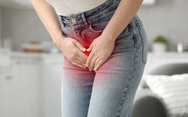 Woman in jeans holding hands over her lower pelvic area indicating bladder discomfort.